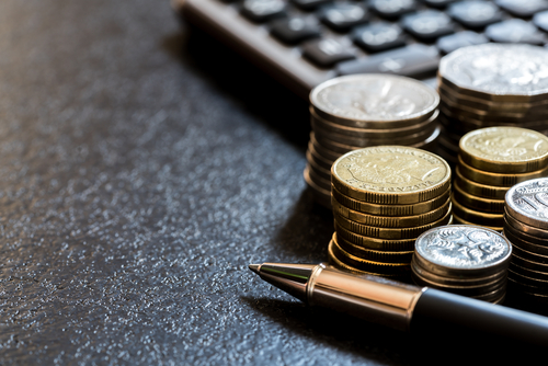 Stacks of coins next to a pen and calculator, symbolising reduced operational costs achieved by using autosteer technology in farming.