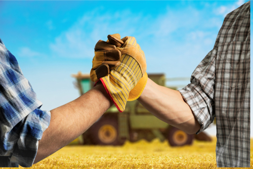 Two farmers shaking hands in a field with a tractor in the background, representing reduced risks of operator fatigue through the use of autosteer technology.