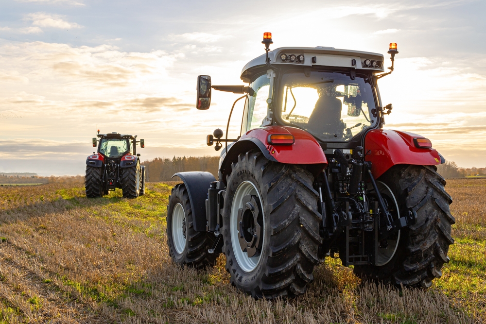 Two red tractors equipped with autosteer for tractors working in a field at sunrise, showcasing the precision and efficiency of autosteer technology for tractors in modern farming.